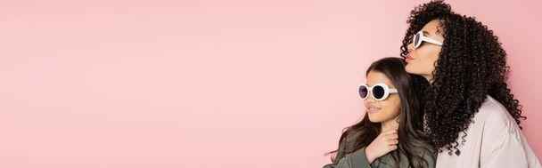 Göndör nő áll közel tizenéves lánya napszemüvegben elszigetelt rózsaszín, banner  - Fotó, kép