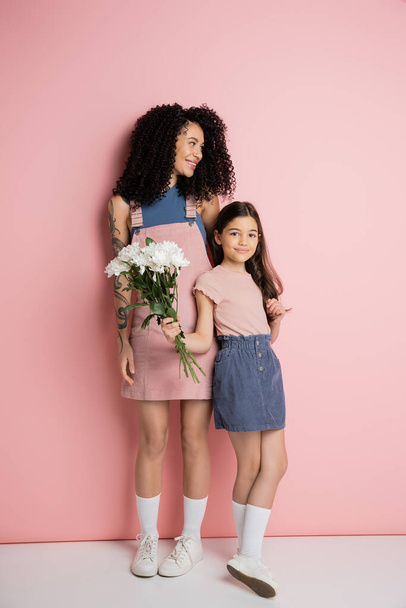 Full length of stylish kid holding bouquet near mom on pink background  - Fotoğraf, Görsel