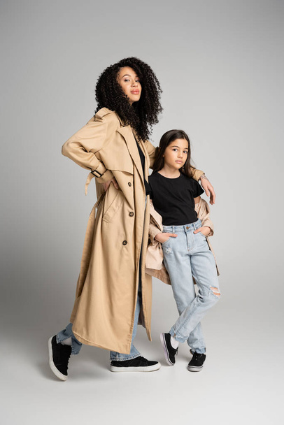 Full length of stylish mother and daughter in trench coats posing on grey background  - Foto, Bild