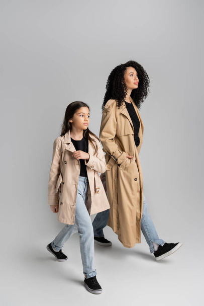 Модна мати і дочка в траншеї пальто ходять на сірому фоні
  - Фото, зображення