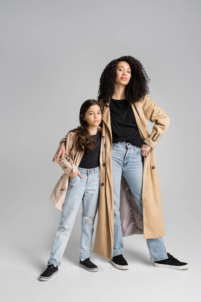 Trendy woman and girl in trench coats looking at camera on grey background  - Photo, image