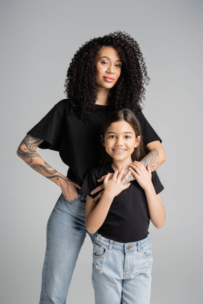 Stylish tattooed woman hugging child in t-shirt isolated on grey  - Foto, imagen
