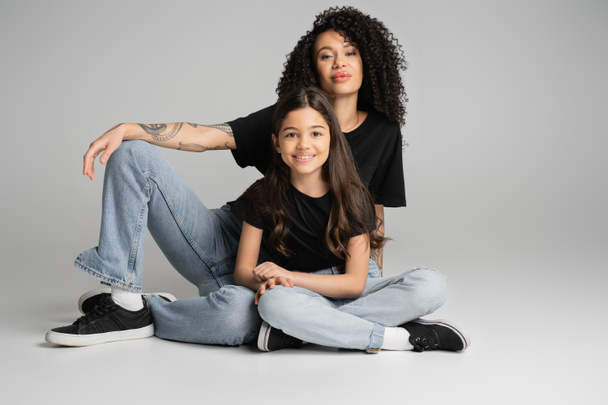 Positive child and mother in jeans and t-shirts posing on grey background  - Photo, image