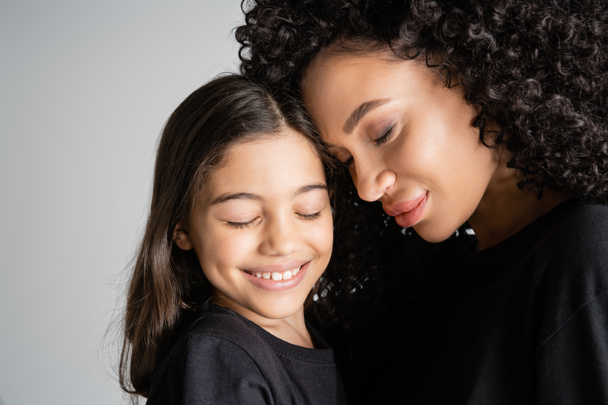 Anyáról és lányáról készült portré fekete pólóban, szürke alapon mosolyogva.  - Fotó, kép