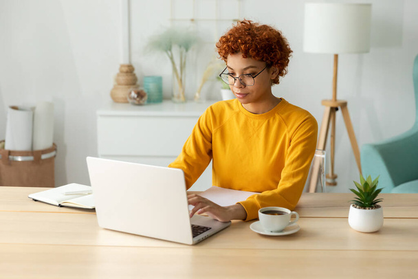 African american girl using laptop at home office looking at screen typing chatting reading writing email. Young woman having virtual meeting online chat video call conference. Work learning from home - Photo, Image