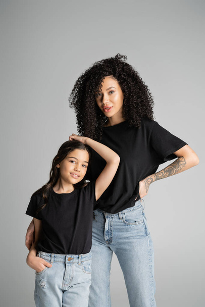 Elegante madre e hija en camisetas negras posando aisladas en gris  - Foto, imagen