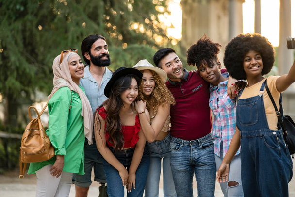 Chicos y chicas multiétnicos tomando selfie al aire libre con retroiluminación - Feliz concepto de amistad estilo de vida acerca de los jóvenes multiculturales divertirse juntos en la ciudad - Foto, Imagen