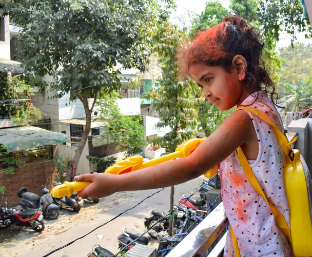 Sweet little Indian girl playing colours on Holi festival, holding pichakaree full of colours, Holi festival celebrations in Delhi, India - 写真・画像