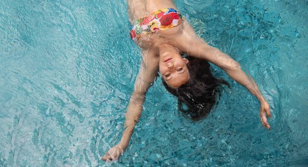top view to young sexy brunette colorful bikini woman swimming in turquoise pool spa water, copy space - 写真・画像