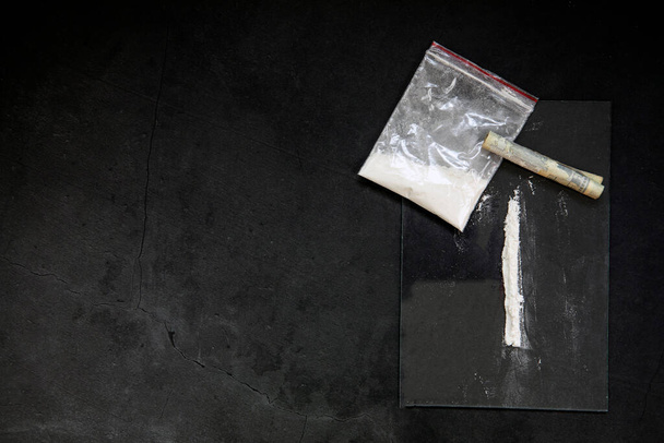 Kokain-Pulverlinien, gerollte Banknoten und Drogen in Plastiktütentasche auf schwarzem Glashintergrund, Draufsicht. Konzept zur Drogenabhängigkeit dunkel - Foto, Bild