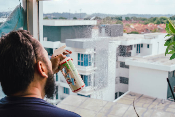 At home, clean the glass balcony. A man of Asian origin is cleaning his home.   - Foto, Imagen