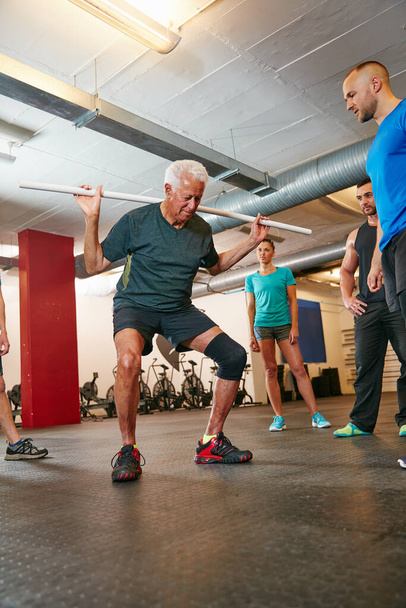 Προσθέστε αυτό το pvc προπόνηση στην εκπαίδευσή σας. ένας ηλικιωμένος που κάνει ασκήσεις PVC ενώ μια ομάδα ανθρώπων παρακολουθεί - Φωτογραφία, εικόνα