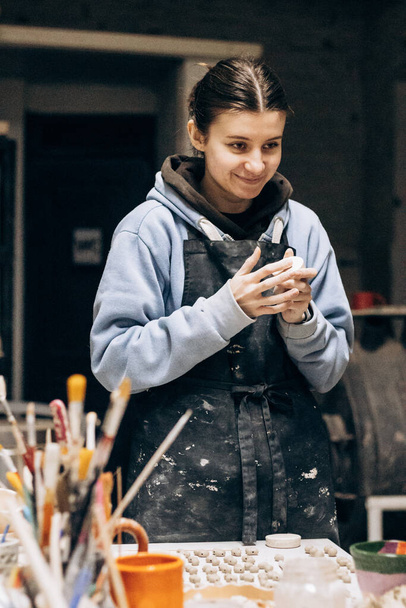 Girl sculpts from clay with the help of tools. Working with raw clay. Female master potter table in workshop With the help of a special tool, removes excess - Foto, Imagem