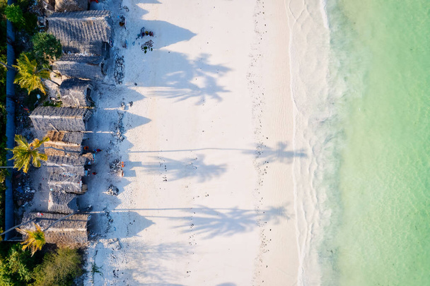 The aerial view of Zanzibar's Indian Ocean coastline is simply stunning, featuring palm trees, white sand, and sparkling blue waters. With luxurious hotels and a tropical landscape, it is the perfect destination for a summer holiday.  - Fotoğraf, Görsel