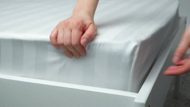A gumiszalagon lévő lap levételének folyamata a matracról. Sávos szatén fehér ágynemű. - Felvétel, videó