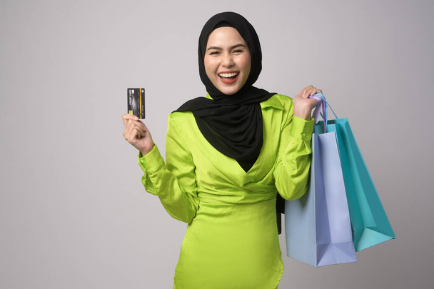 A Beautiful musllim woman with hijab holding credit card and shopping bag over white background studio, shopping and finance concept. - Foto, immagini