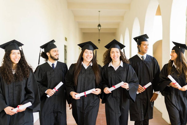 Feliz grupo de amigos riendo y caminando después de recibir su diploma universitario en su ceremonia universitaria - Foto, imagen