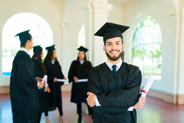 Atractivo graduado mexicano en un campus universitario con un vestido de graduación después de recibir su diploma universitario - Foto, Imagen