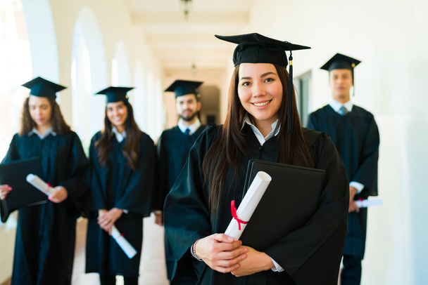 Caucasica donna attraente in possesso del suo diploma di college sorridente guardando la fotocamera indossa il suo abito di laurea - Foto, immagini