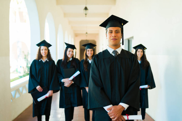 Красивий іспаномовний чоловік випускник стоїть з друзями в кампусі після закінчення навчання в коледжі
 - Фото, зображення