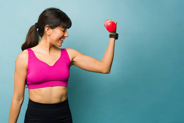 Lächelnde Fitness-Frau sieht glücklich aus, während sie Hantelgewichte hebt und Bizeps-Locken macht - Foto, Bild