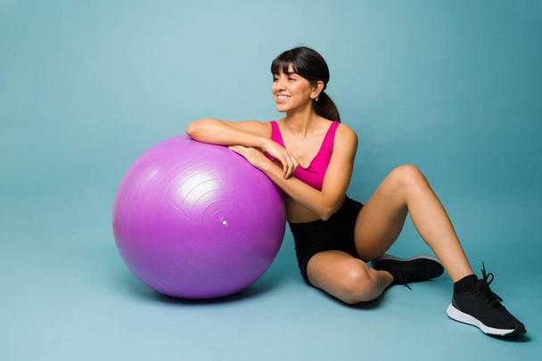 Hermosa mujer joven y entrenamiento entrenador de fitness con una pelota de estabilidad contra un fondo de estudio azul - Foto, Imagen