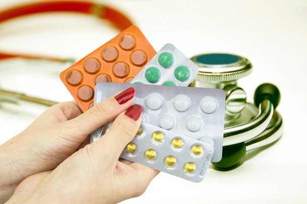 Multi-gekleurde tabletten in handen op stethoscoop - Foto, afbeelding