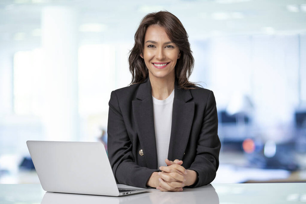 Attractive businesswoman wearing blazer and using laptop for work. Smiling female looking at camera and smiling.  - Foto, afbeelding