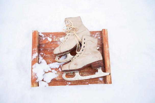 Viejos patines vintage en la nieve.Un par de patines blancos en un tablero cubierto de nieve de madera. - Foto, imagen