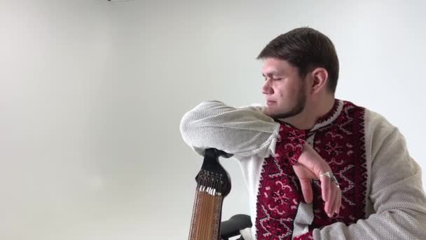 starke ukrainische Kosaken in einem bestickten Hemd Rotes Kreuz-Stich auf weißem Leinen lehnte an einem Musikinstrument Bandura und blickt in die Ferne mit traurigem Blick zuversichtlich Stärke des Mutes Held - Filmmaterial, Video