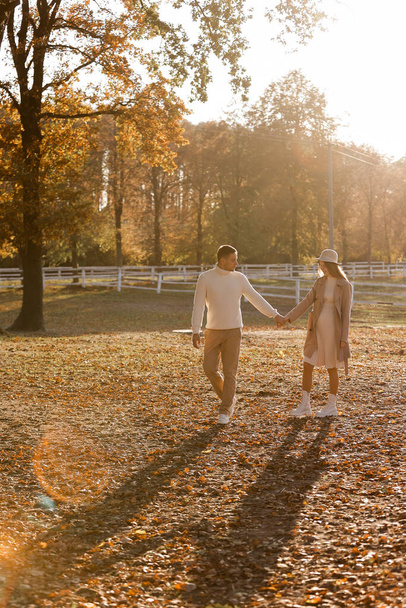 Jong stel, man en zwangere vrouw houden elkaars hand vast en wandelen in het herfstpark bij zonsondergang. Gelukkige familie geniet van zwangerschap op de natuur. Het concept van moederdag en vrouwendag. kopieerruimte. - Foto, afbeelding