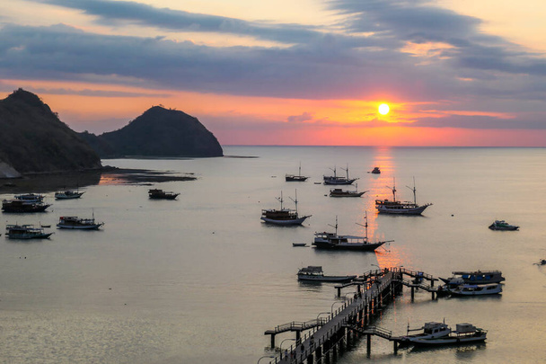 Вид на гавань в Лабуан-Бахо, Флорес, Індонезія під час заходу сонця. Сонце сідає за лінію горизонту. Багато човнів стоять на якорі до берега. На задньому плані мало островів. Золота година у гавані - Фото, зображення