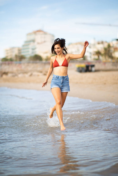 Ganzes Porträt einer unbeschwerten jungen Frau, die am Strand läuft - Foto, Bild