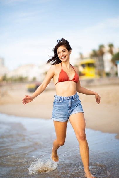 Täyspitkä muotokuva hymyilevä nuori nainen käynnissä rannalla - Valokuva, kuva