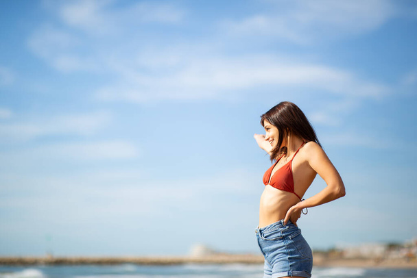 Side portrait of attractive young woman standing on beach during vacation - Photo, image