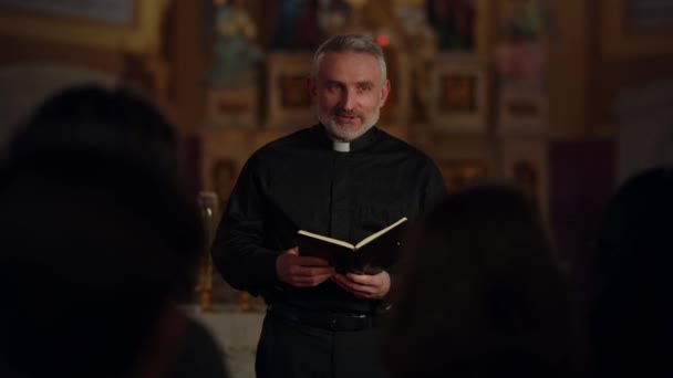 A priest in a black robe stands in front of the people during the Sunday service. The priest reads a passage from the Bible to the parishioners. High quality 4k footage - Filmmaterial, Video