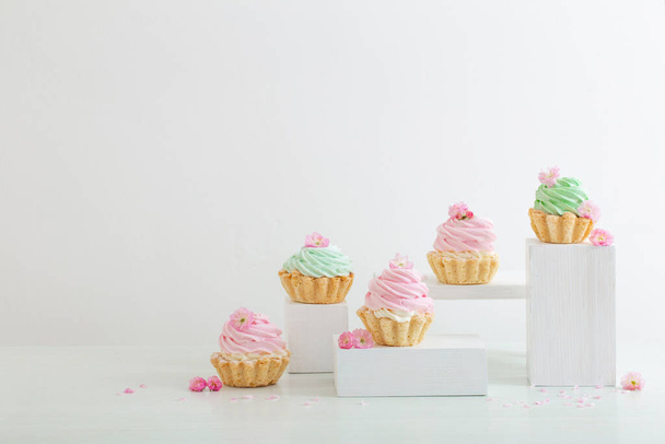 pink and green cupcakes with spring flowers  on wooden podiums on white  background - Φωτογραφία, εικόνα