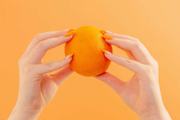 mão feminina com laranja sobre fundo laranja - Foto, Imagem