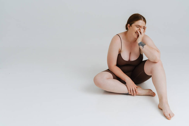 European woman with ginger hair laughing while sitting on floor isolated over white background - Valokuva, kuva