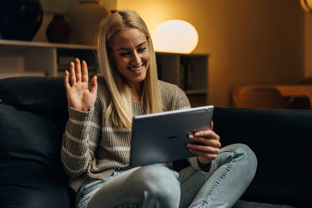 A woman is waving to the camera on tablet during a video call - Foto, afbeelding