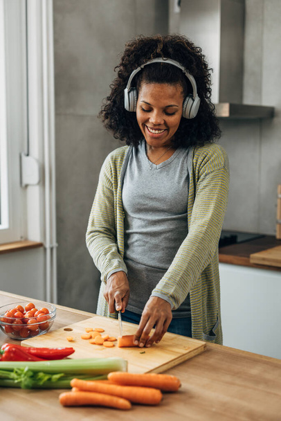 Joyful mixed race woman is chopping carrots - Foto, Imagen