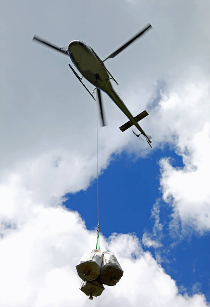 Вертоліт у польоті під час транспортування вантажів, прикріплених до лебідки та сталевого кабелю
 - Фото, зображення