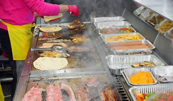 Кухарі, які готують вуличну їжу з м'ясом і овочами в гарячій металевій тарілці в кабінці на ярмарку
 - Фото, зображення