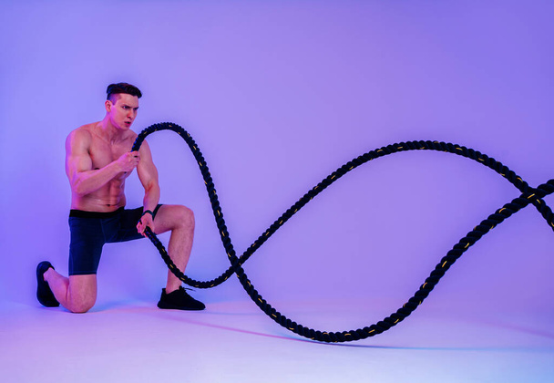 Athletic man with fit muscular body training in studio - Active man doing a workout, colorful lighting and background, concepts about fitness, sport and health lifestyle - Foto, Imagen