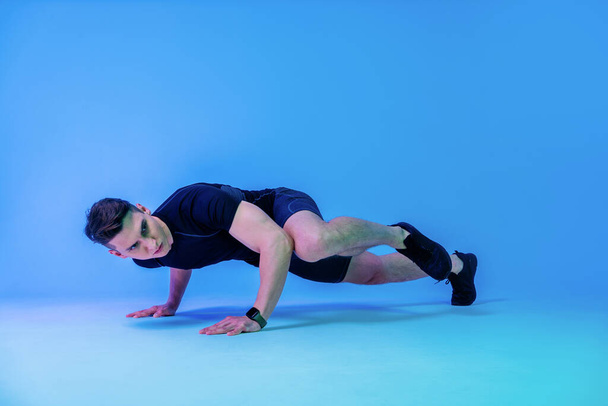 Atletyczny mężczyzna z dopasowanym muskularnym treningiem ciała w studio - Aktywny człowiek wykonujący trening, kolorowe oświetlenie i tło, koncepcje fitness, sportu i zdrowia stylu życia - Zdjęcie, obraz