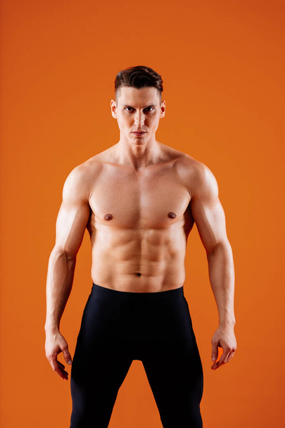 Atletyczny mężczyzna z dopasowanym muskularnym treningiem ciała w studio - Aktywny człowiek wykonujący trening, kolorowe oświetlenie i tło, koncepcje fitness, sportu i zdrowia stylu życia - Zdjęcie, obraz