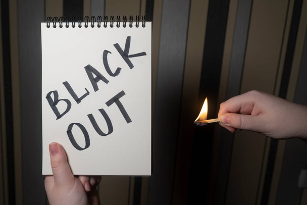 Notepad with the inscription "Blackout" in one hand and burning matches in the other hand (close-up). Power outage concept. Energy crisis - Photo, Image