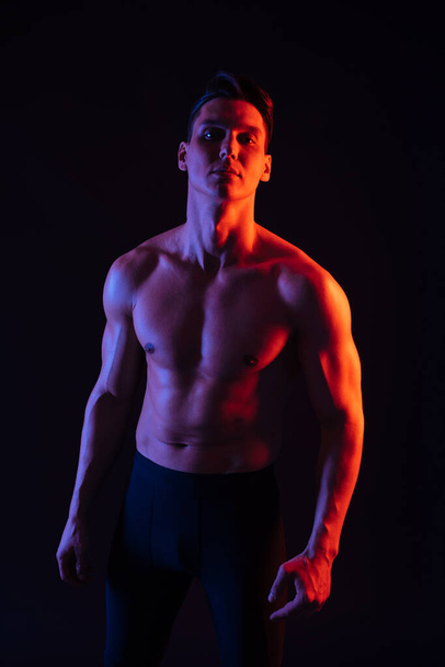 Sportos férfi fitt izmos test képzés stúdióban - Aktív férfi csinál egy edzés, színes világítás és a háttér, fogalmak fitness, sport és egészségügyi életmód - Fotó, kép