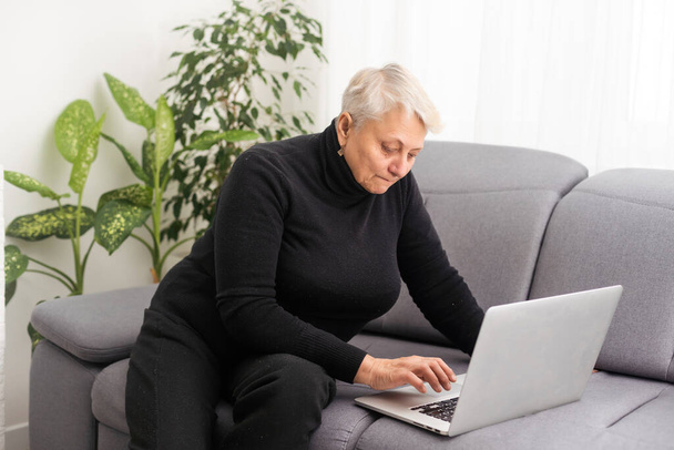 Вид спереди сконцентрировал приятную зрелую женщину постарше, смотрящую на экран компьютера. Счастливая дама средних лет занимается веб-серфингом, заказывает еду онлайн, читает в социальных сетях, играет в игры
. - Фото, изображение