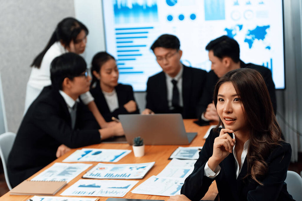 Focus portrait of female manger, businesswoman in the harmony meeting room with blurred of colleagues working together, analyzing financial paper report and dashboard data on screen in background. - 写真・画像